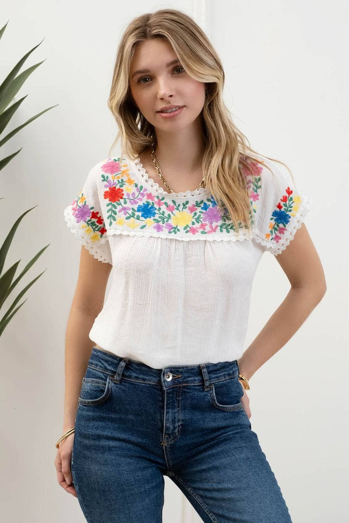 tucked in view of Whitney Floral Embroidery Blouse with a round neckline, short sleeves, and scallop lace trim. Made from 86% rayon and 14% nylon with a contrast of 100% polyester.