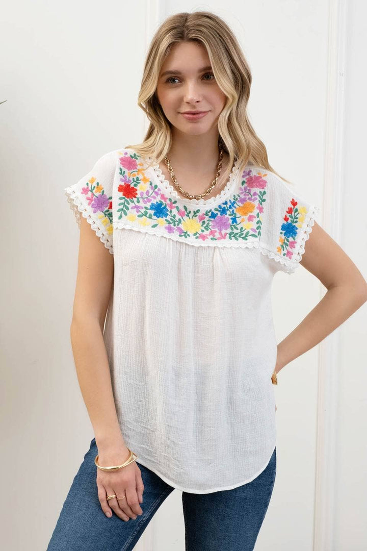 styled view of Whitney Floral Embroidery Blouse with a round neckline, short sleeves, and scallop lace trim. Made from 86% rayon and 14% nylon with a contrast of 100% polyester.