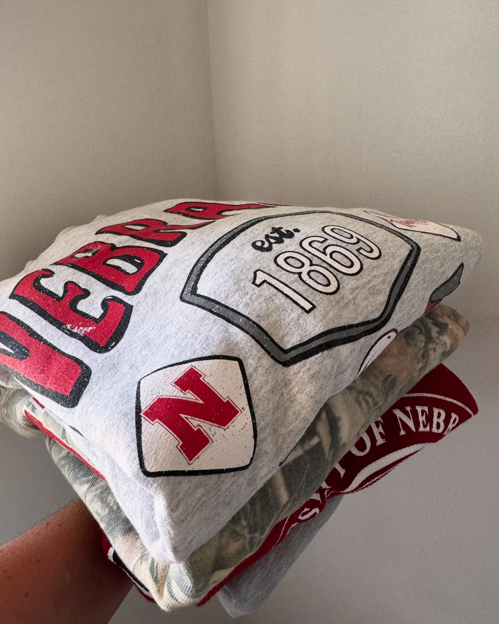 folded Nebraska Huskers Patches Sweatshirt — distressed thrifted ash gray crew, unisex fit, officially licensed graphic by Onyx Native