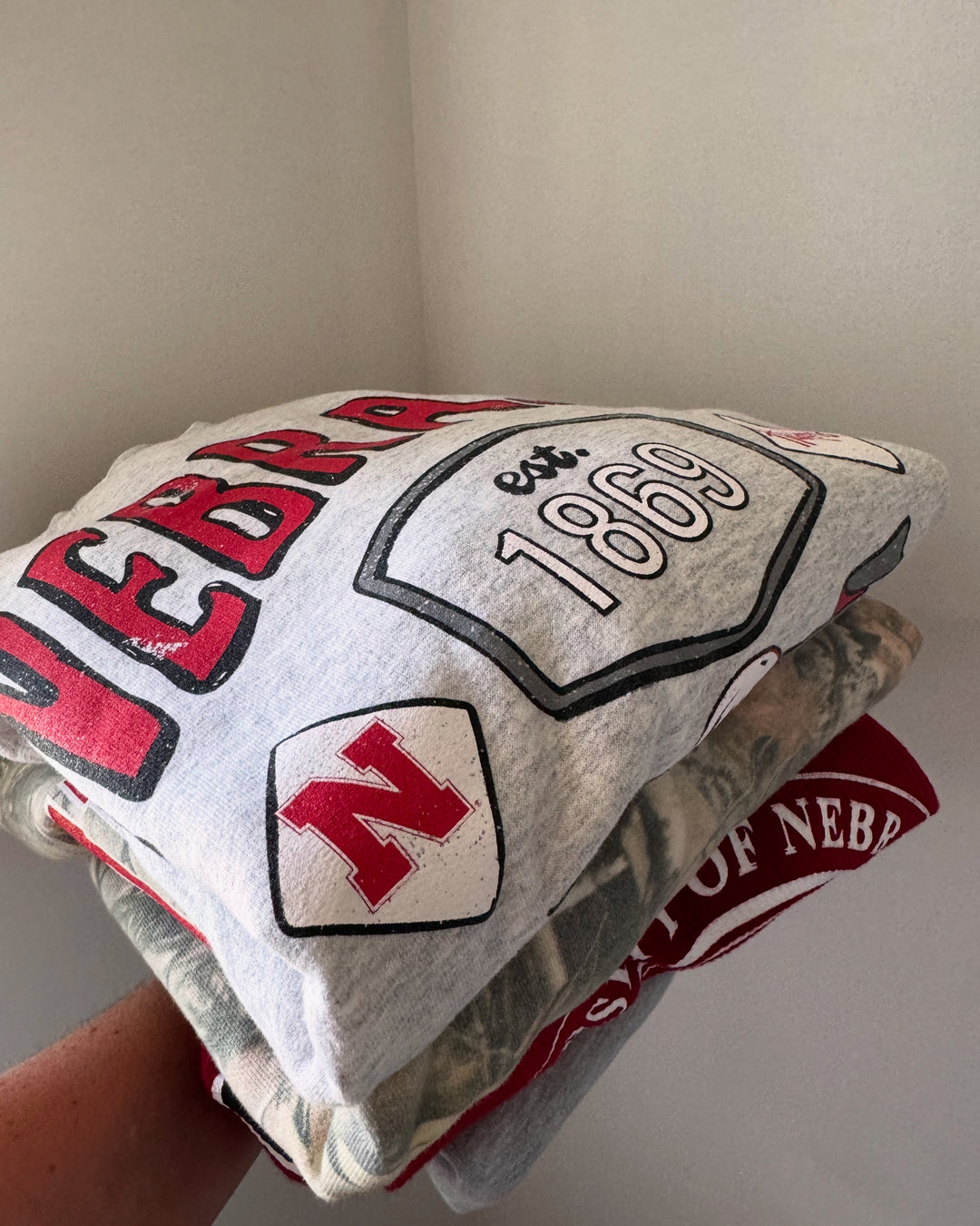 folded Nebraska Huskers Patches Sweatshirt — distressed thrifted ash gray crew, unisex fit, officially licensed graphic by Onyx Native