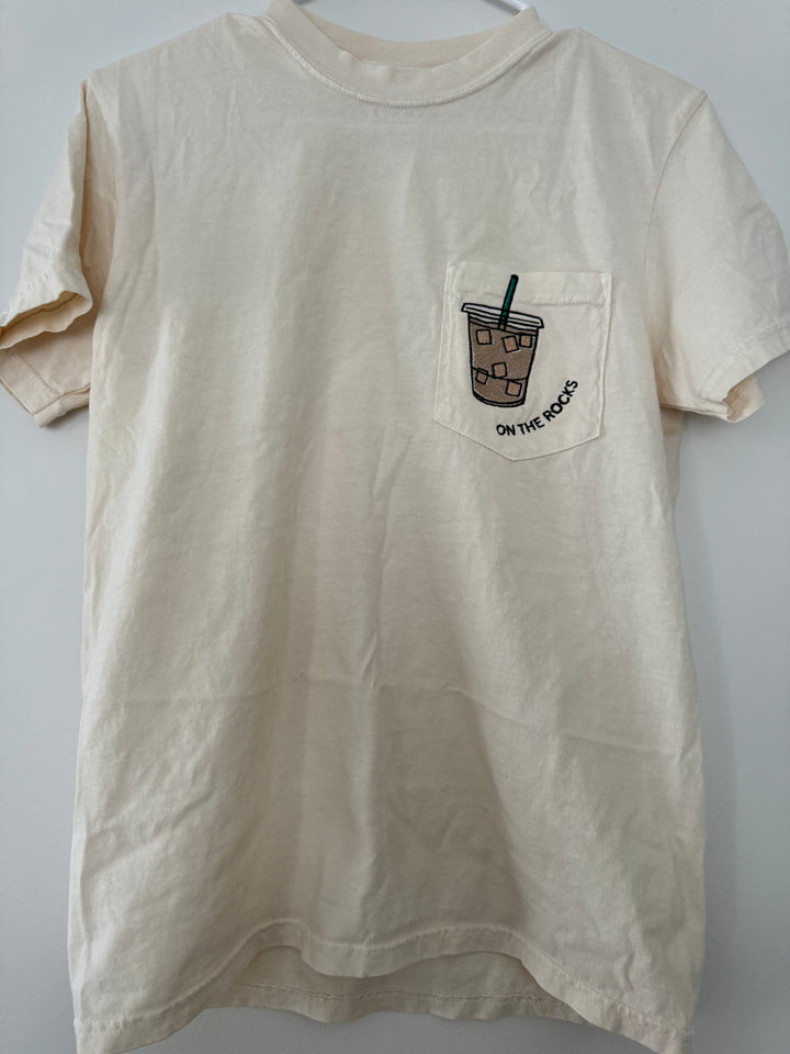 hanger view of 'On the Rocks' Embroidered Pocket Tee in cream with custom colors. Perfect for coffee lovers.