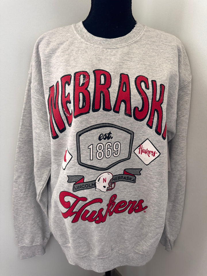 Nebraska Huskers Patches Sweatshirt — distressed thrifted ash gray crew, unisex fit, officially licensed graphic by Onyx Native