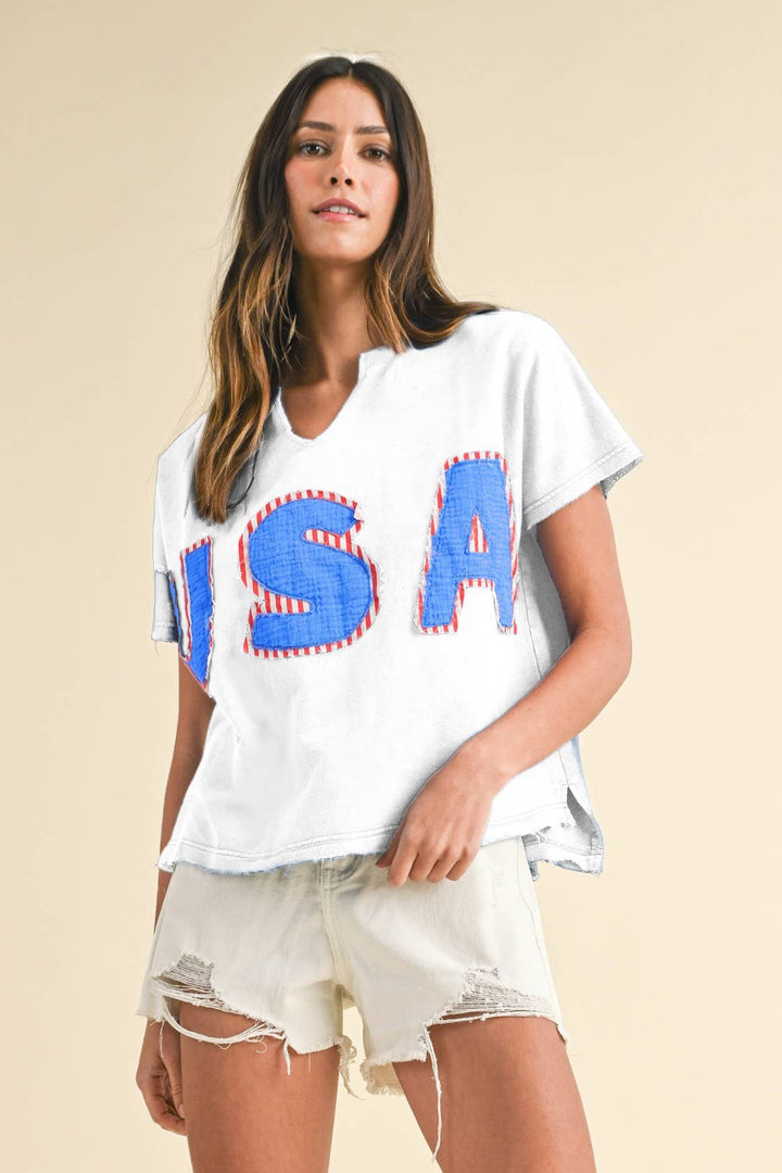 white colored Mineral Washed USA Patched Knit Top with mixed fabric lettering patch, lightweight French terry, notched neckline, short dolman sleeves, raw edge details, and loose fit.