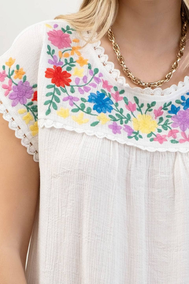 detailed view of Whitney Floral Embroidery Blouse with a round neckline, short sleeves, and scallop lace trim. Made from 86% rayon and 14% nylon with a contrast of 100% polyester.