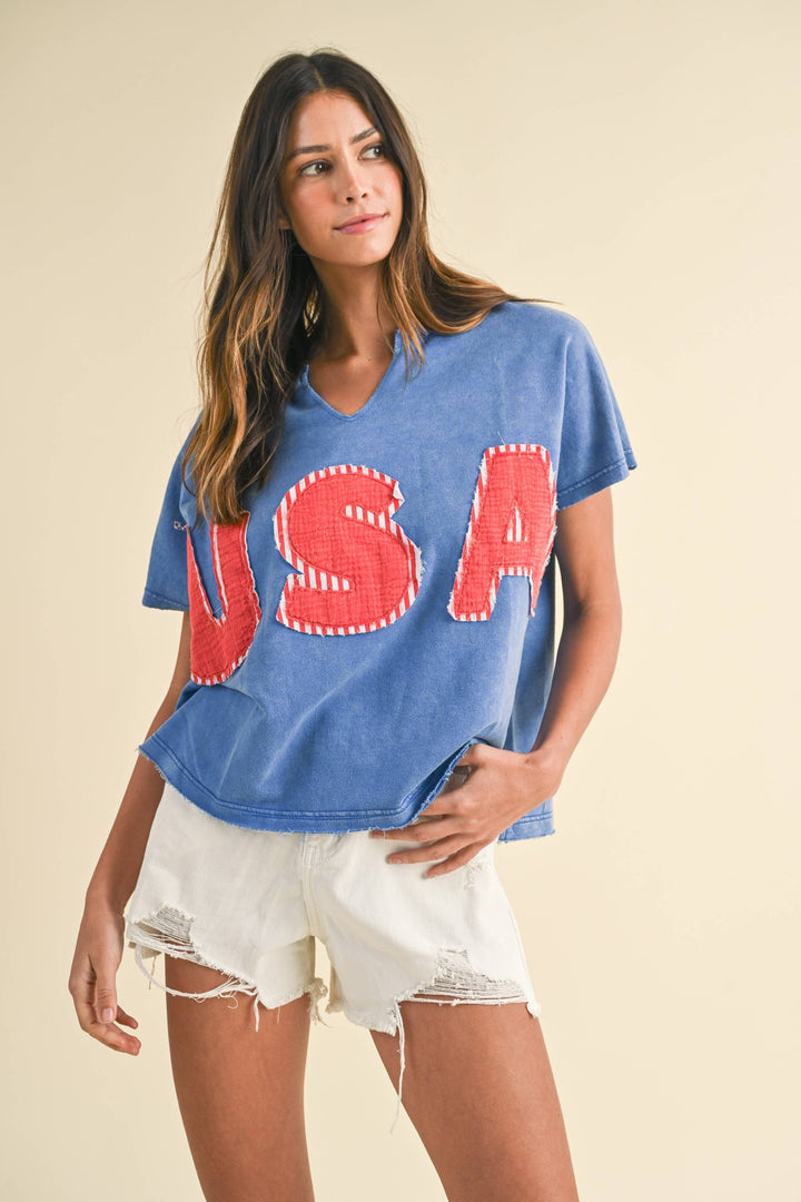 styled view of Mineral Washed USA Patched Knit Top with mixed fabric lettering patch, lightweight French terry, notched neckline, short dolman sleeves, raw edge details, and loose fit.