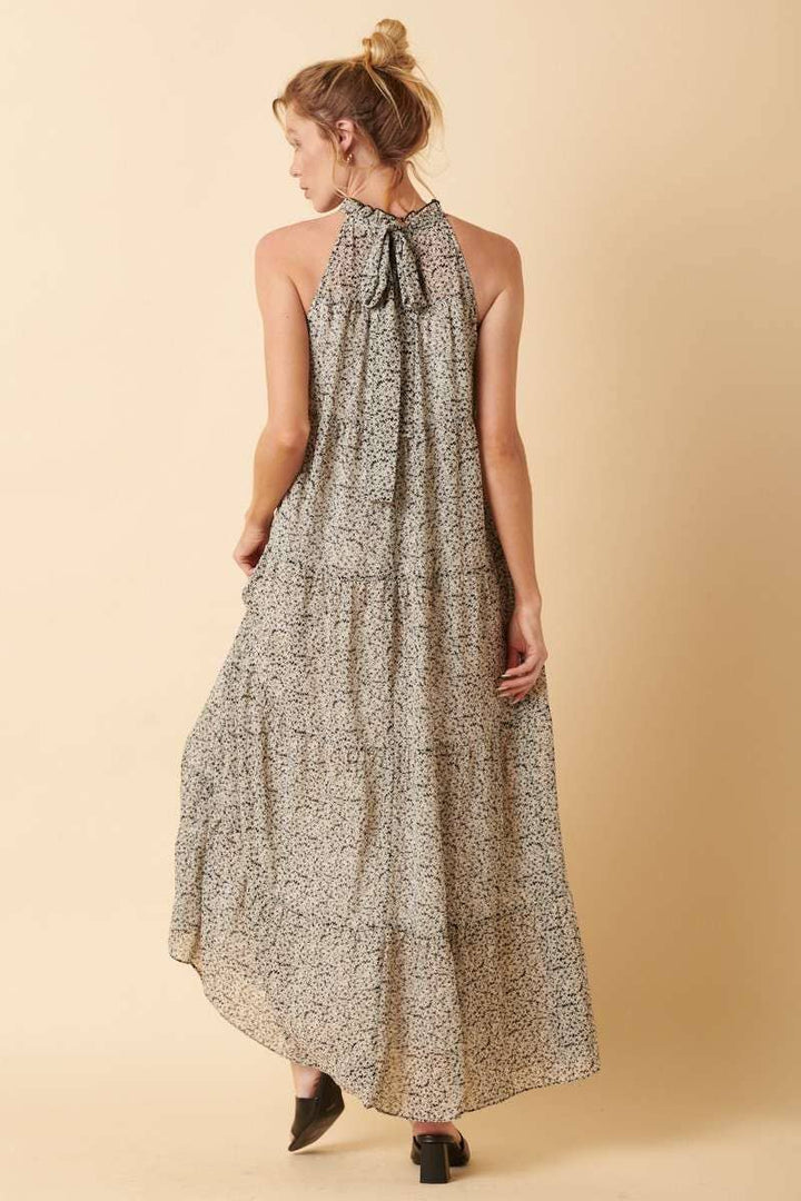 back view of Sally Flower Halter Maxi Dress with flower print on chiffon fabric, ruffle mock neck, tie back, sleeveless halter design, and tiered detail. Maxi length for an elegant silhouette.