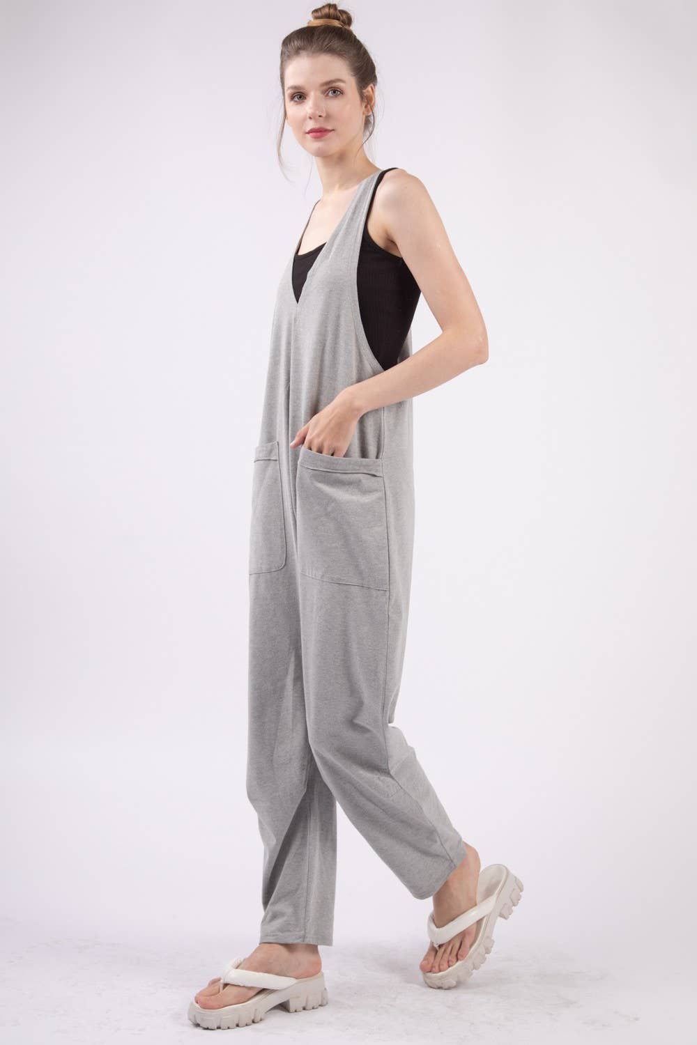 slight left side view of Casual loose fit solid knit baggy jumpsuit with a deep V-neck, sleeveless design, raw edge detail, and side pockets. 