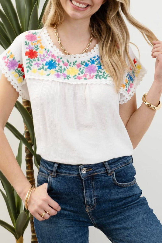 Whitney Floral Embroidery Blouse with a round neckline, short sleeves, and scallop lace trim. Made from 86% rayon and 14% nylon with a contrast of 100% polyester.