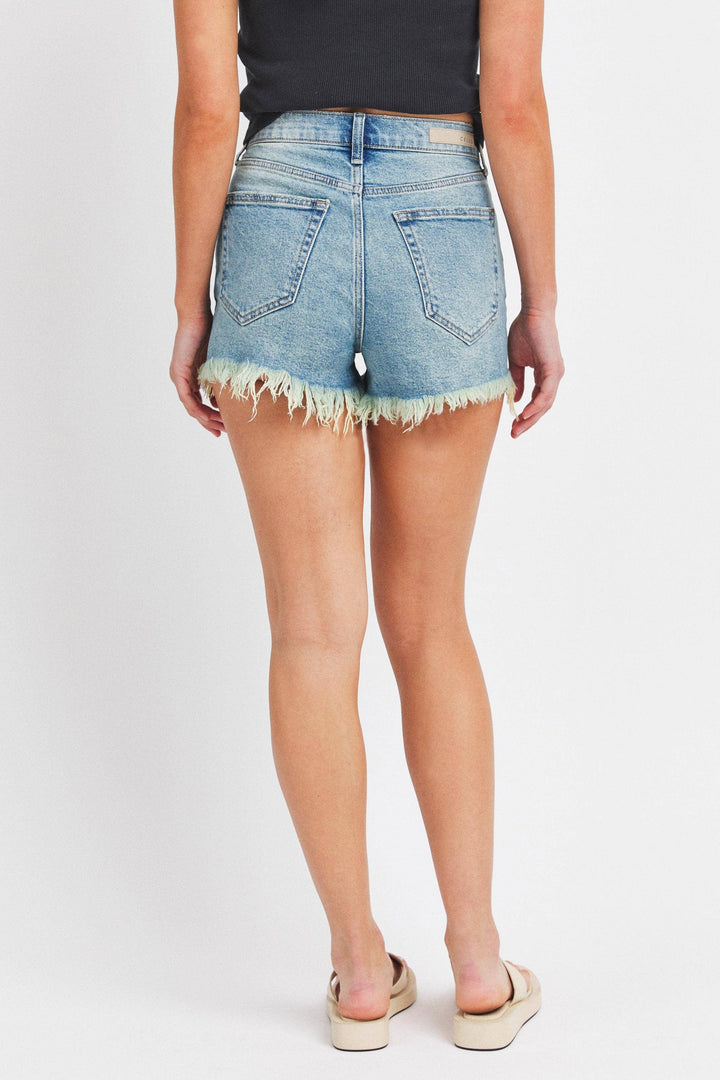 back view of High Rise Mom Shorts in tinted denim with a frayed hem, high-waist design, belt loops, and zip fly. Made from 99% cotton and 1% spandex.