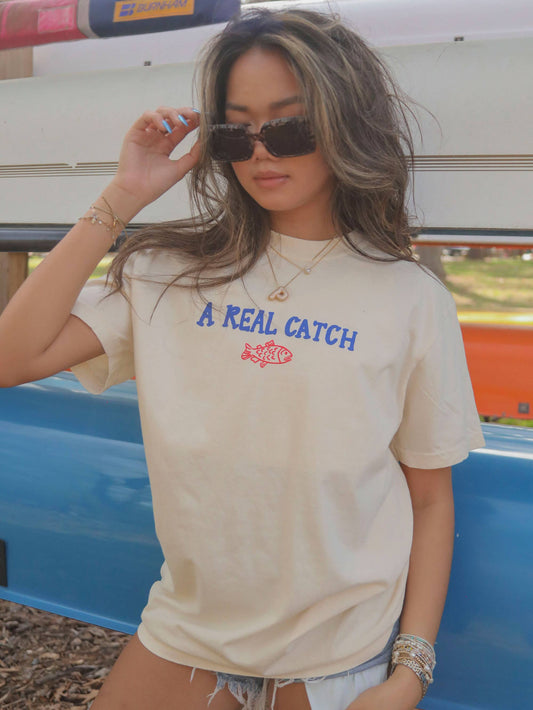 Americana-inspired graphic tee with 'Catch of the Day' text. Features a fun, lake-themed graphic perfect for boaters and fishing enthusiasts.