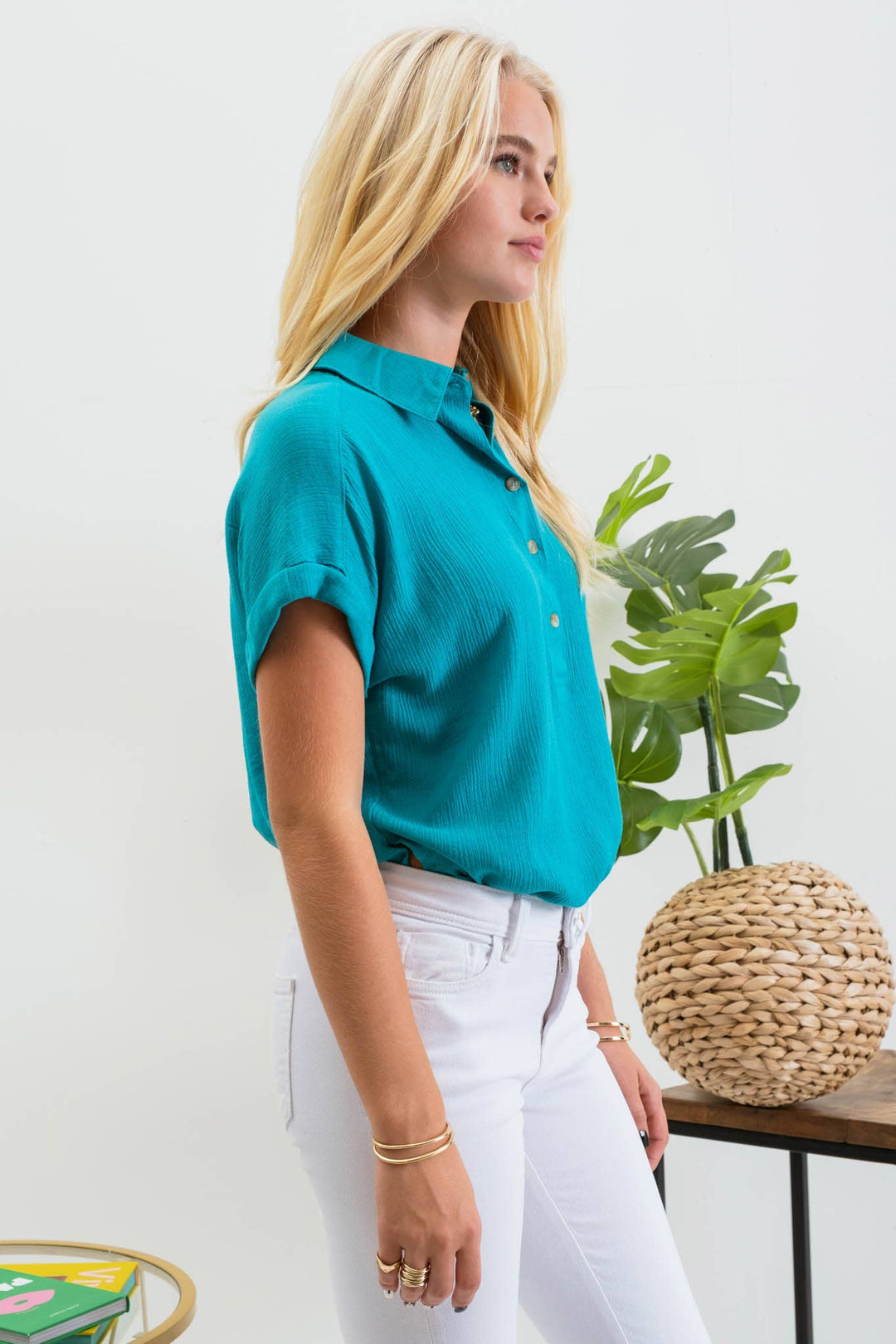 side view of Mid Button Down Woven Top with pointed collar, front functional buttons, folded cuff short sleeves, back yoke, and shirring detail. Made of 80% rayon and 20% nylon.