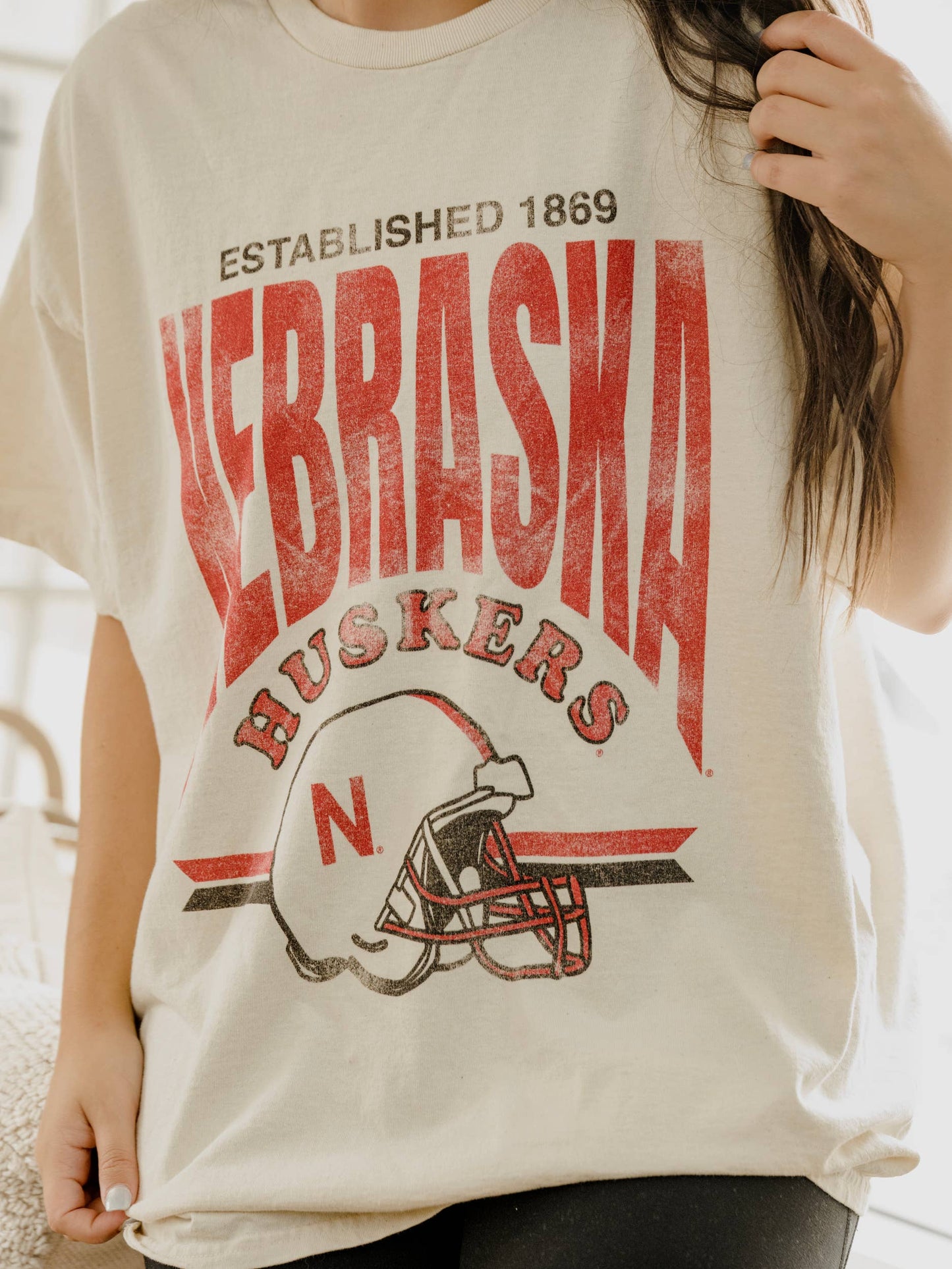 zoomed in view of Nebraska Established Date Helmet Off White Thrifted Tee, 100% preshrunk cotton, unisex fit, meaningfully distressed, and officially licensed with unique colors and distressing.