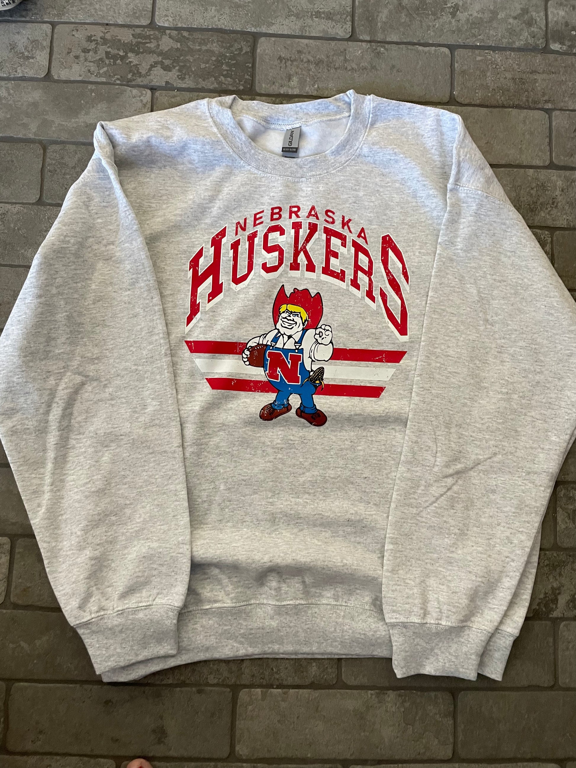 zoomed out view of Nebraska Huskers Football crewneck sweatshirt in a 50/50 cotton-poly blend. Features pre-shrunk fabric, classic fit, air-jet spun yarn for softness, and double-needle stitching for durability. Ideal for staying warm in colder months.