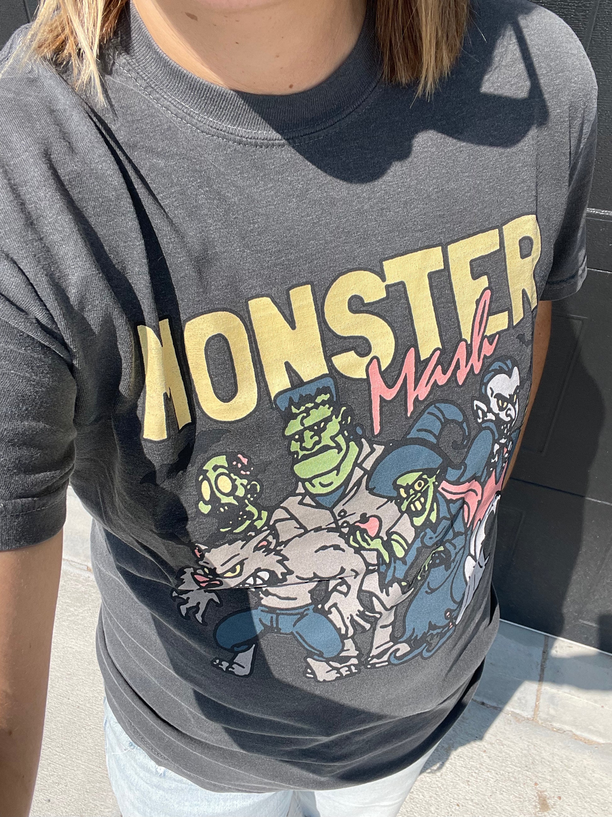 zoomed in view of Monster Mash pigment dyed tee in pepper color with heat-pressed decoration. Made from 100% US ring spun cotton with a soft-washed, garment-dyed finish, featuring a classic rib collar and double-needle hems.