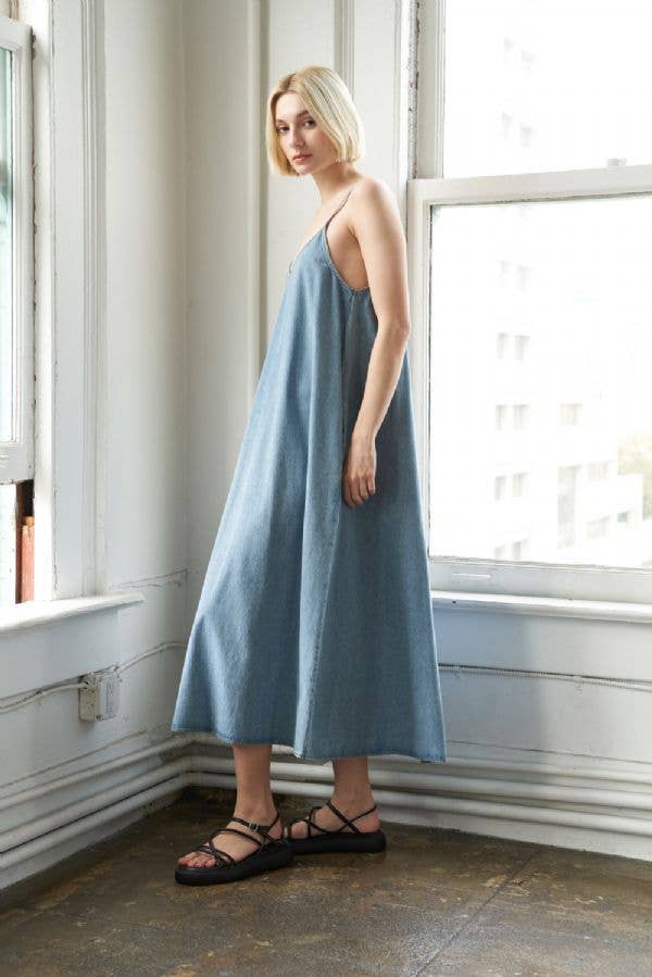 left view of Washed denim midi dress with side pockets and straps. Made from 85% cotton, 10% polyester, and 5% viscose. Approx. length 52 inches. 