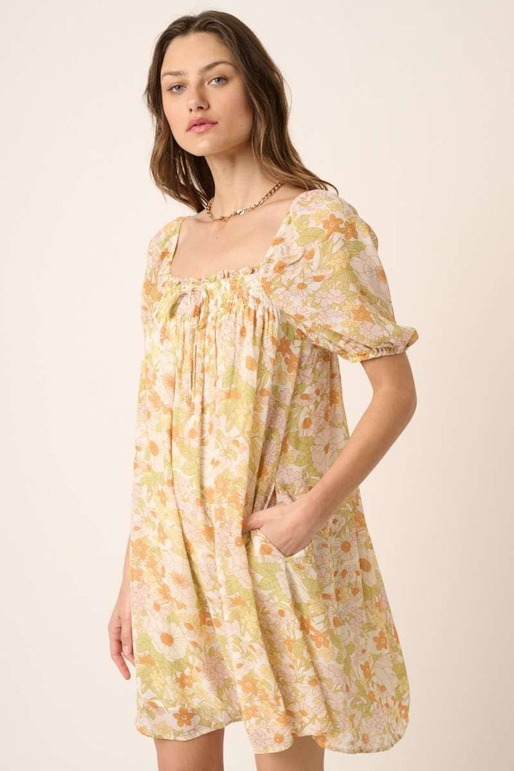 hand in pocket view of Vintage Flower Print Mini Dress with square neck, short puff sleeves, and tie detail on top. Made from chiffon woven fabric and fully lined. Model is 5'9" wearing size Small.