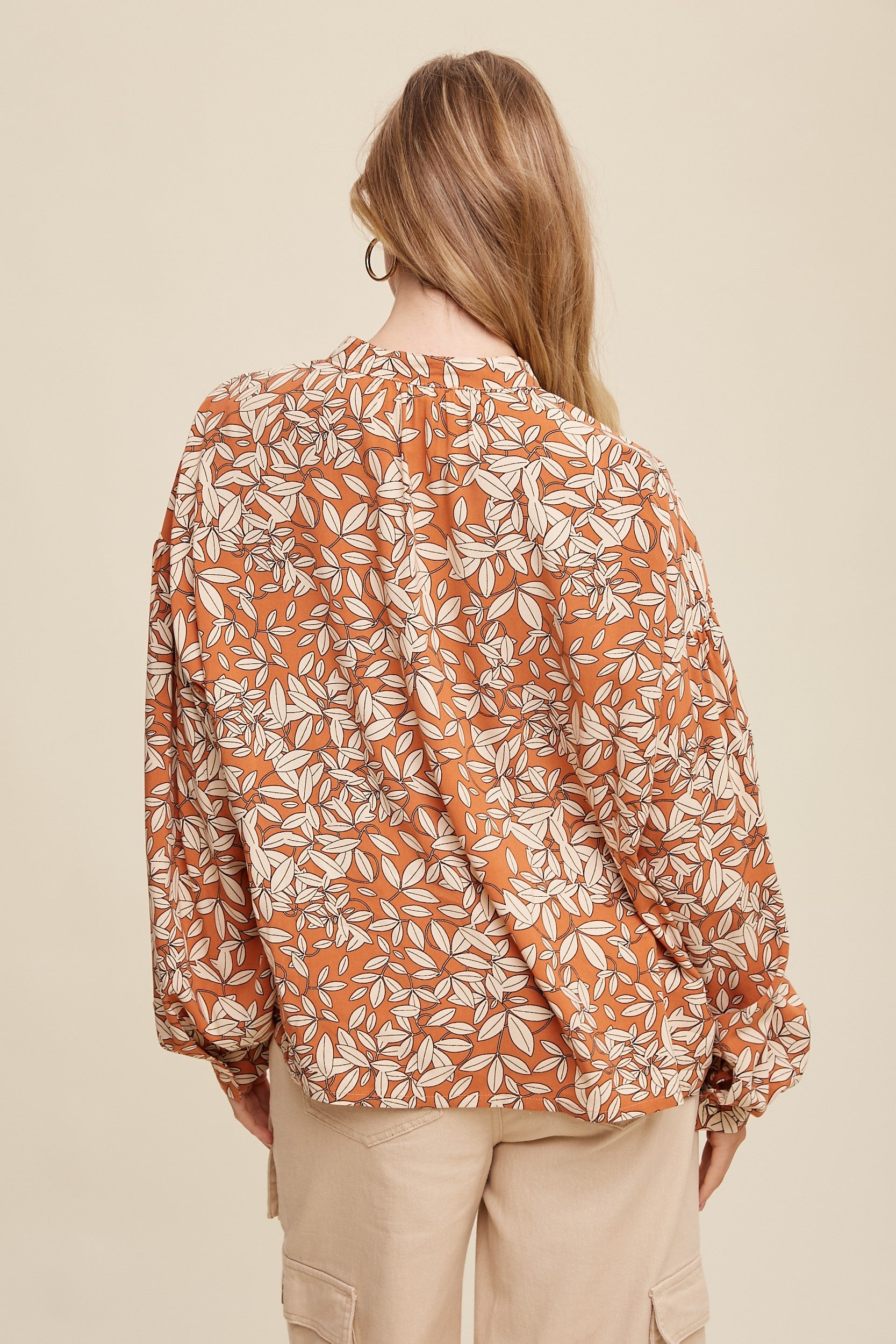 back view of Leaf print blouse with button-down front and long puff sleeves with button closures at the cuffs. Features a clean, curved hem for a polished look.