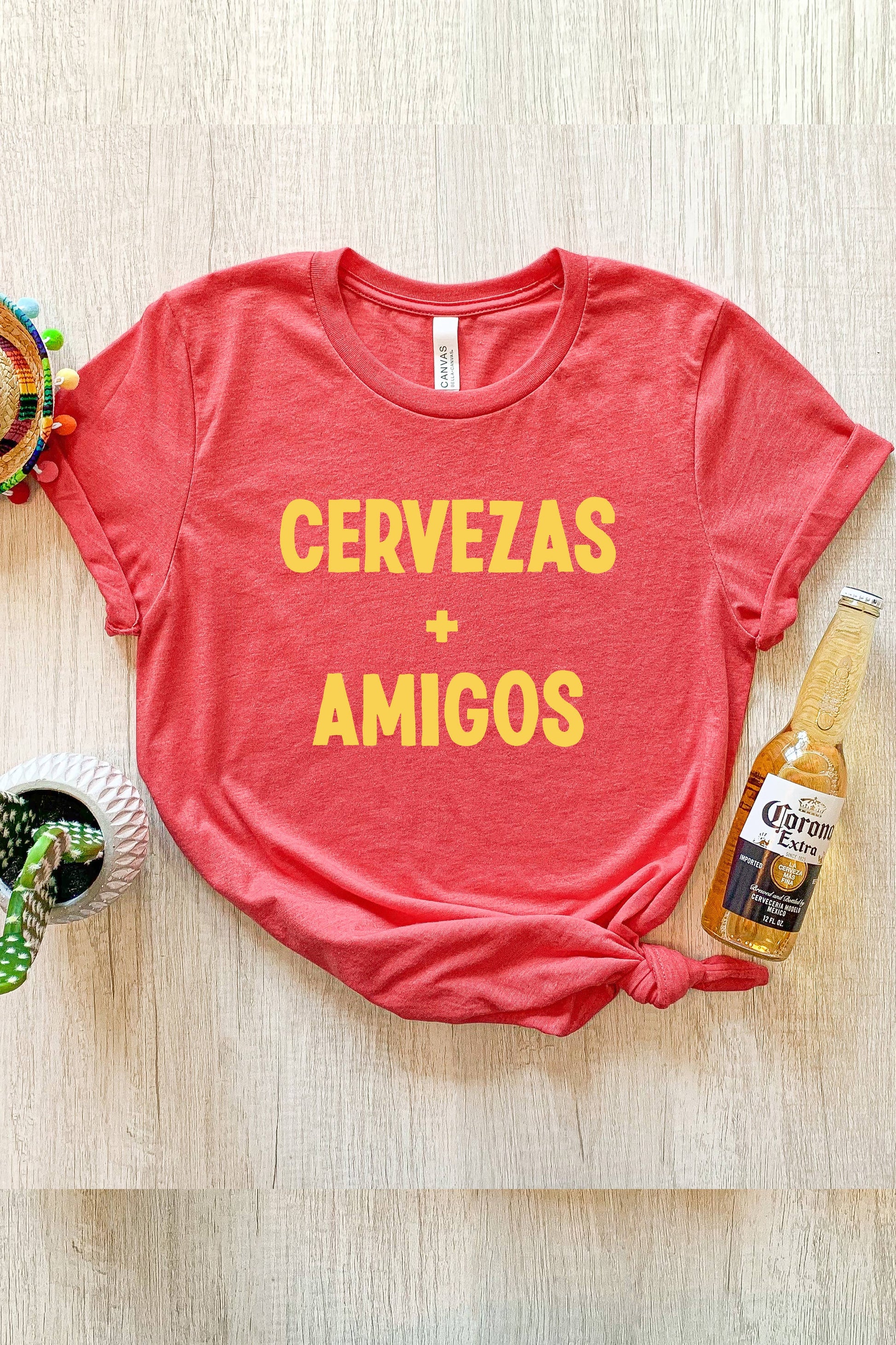 Red graphic tee with 'CERVEZAS + AMIGOS' text printed on it. Features a slim, comfortable unisex fit and is made from 100% airlume combed and ringspun cotton. Printed using DTG on Bella Canvas.